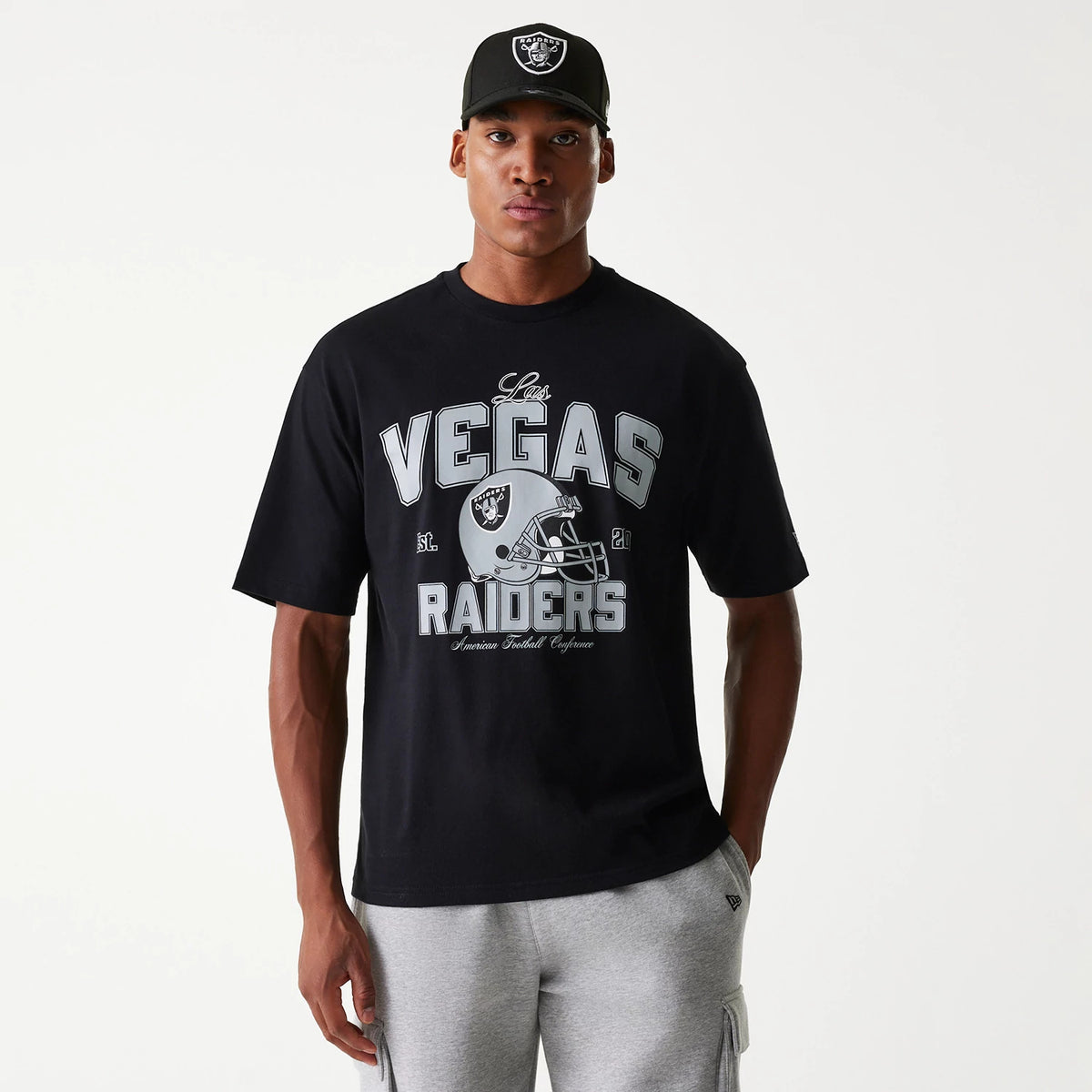 New Era Las Vegas Raiders NFL Helmet Black Oversized T-Shirt, on-model view showing a large front graphic of a silver helmet with the Raiders logo, grey lettering spelling out Vegas Raiders, and a small New Era logo on the sleeve.