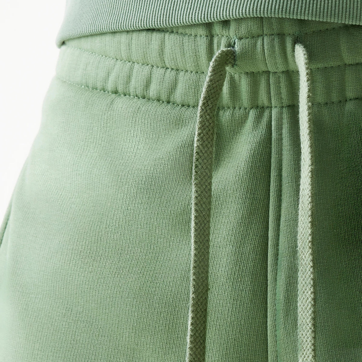 New Era Essential Green Oversized Shorts, side view showing the elastic waistband with matching green drawstrings and detailed stitching along the hip area.