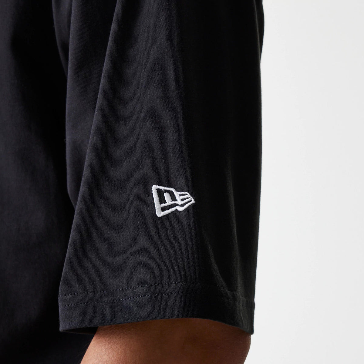 New Era New York Yankees MLB League Essential Black Oversized T-Shirt, side view showing the black short sleeve with a white embroidered New Era logo near the hem and the soft drape of the fabric.