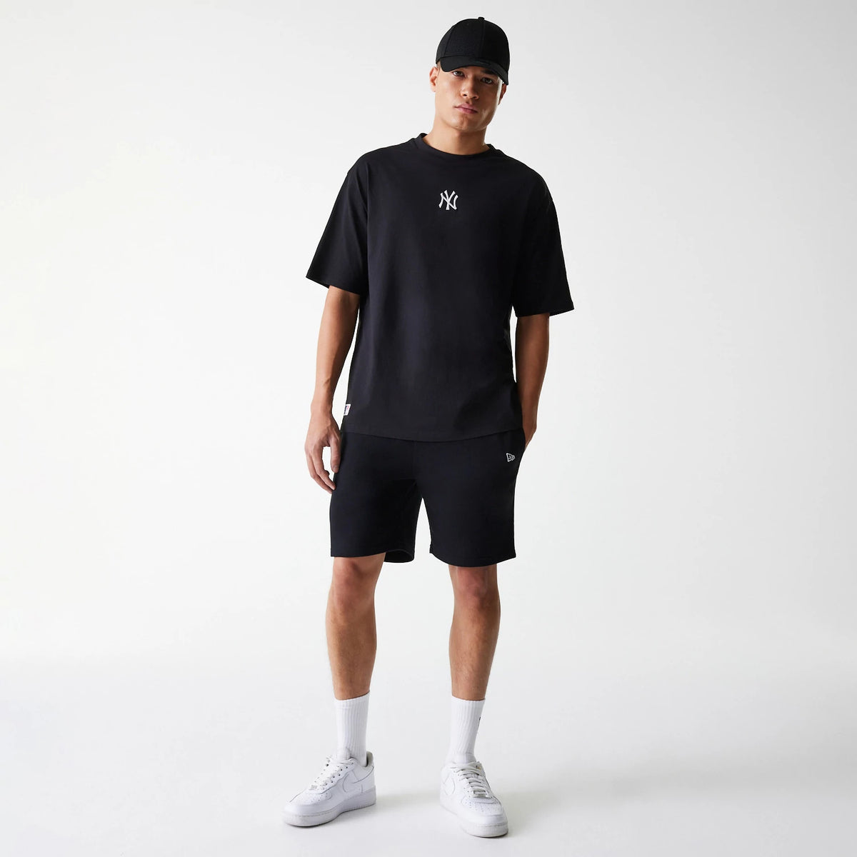 New Era New York Yankees MLB League Essential Black Oversized T-Shirt, on-model view showing the black oversized T-shirt with a white embroidered New York Yankees logo on the chest, paired with black shorts and a black cap.