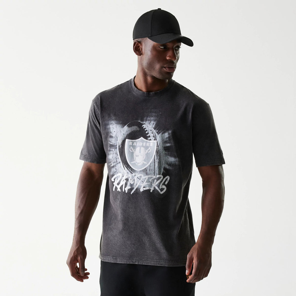New Era Las Vegas Raiders NFL Sport Night Black T-Shirt, front view showing a bold white Raiders logo and text on the chest of the washed black short-sleeve tee worn by a model with a plain black cap.