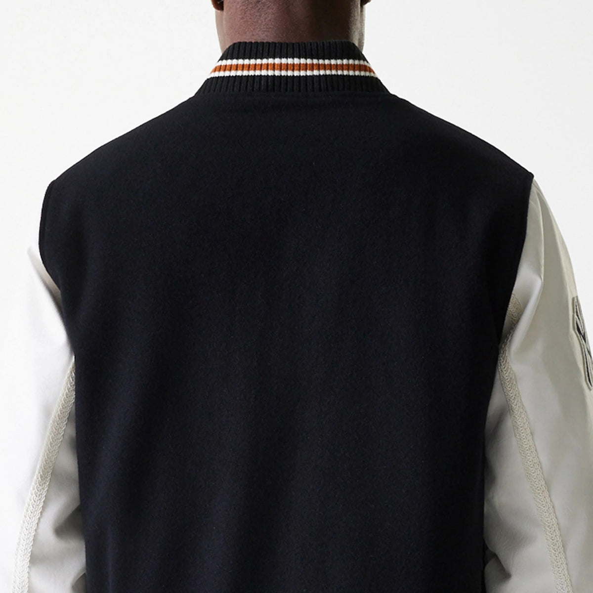 New Era New York Yankees MLB Wordmark Black Varsity Jacket, rear view showing the black body with contrasting white sleeves, an orange and white striped collar, and a raised New Era logo on the upper left sleeve.