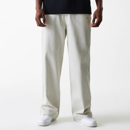 New Era New York Yankees MLB Light Beige Chino Trousers, front view on a model wearing a black top and white sneakers, showing the relaxed fit and the New Era flag logo embroidered on the left pocket area.
