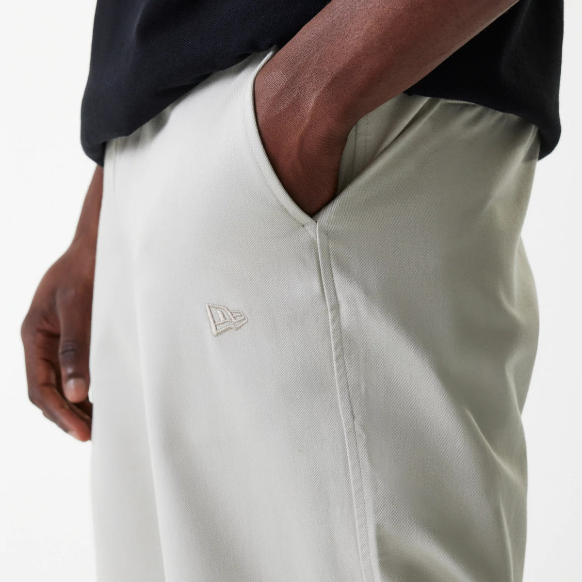 New Era New York Yankees MLB Light Beige Chino Trousers, side view on a model with hands in pockets, featuring the embroidered New Era flag logo on the left thigh near the side seam.