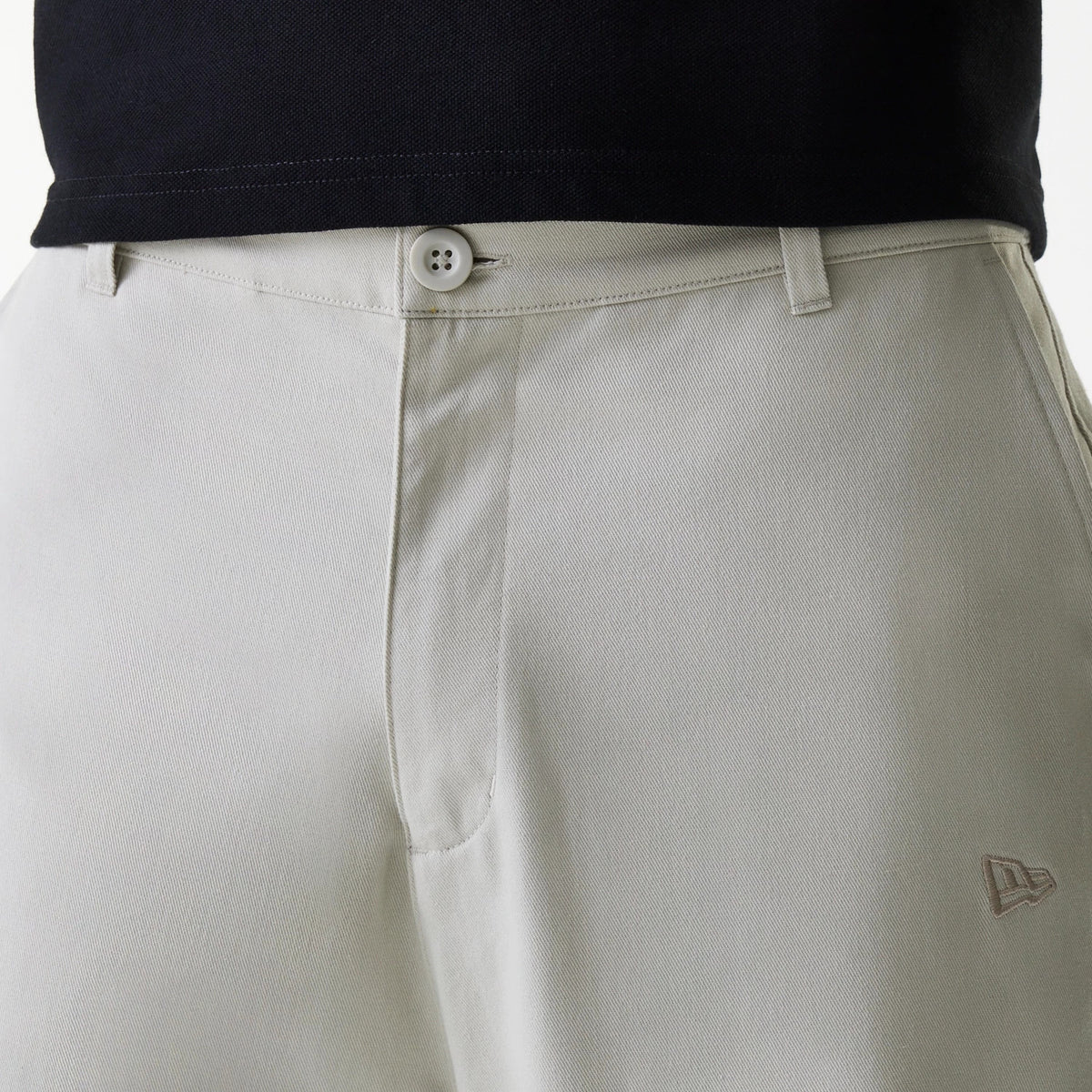 New Era New York Yankees MLB Light Beige Chino Trousers, front view showing the New Era flag logo embroidered in light beige on the right thigh, flat waistband with belt loops and a button closure, styled with a black shirt.
