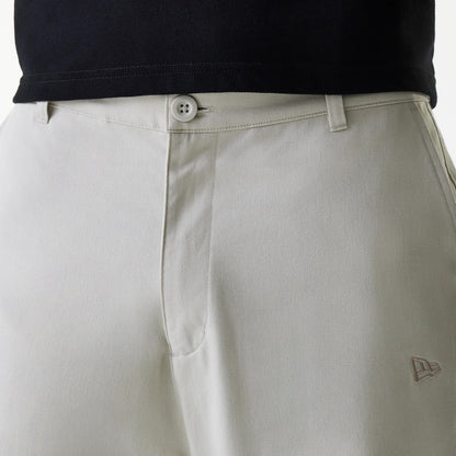 New Era New York Yankees MLB Light Beige Chino Trousers, front view showing the New Era flag logo embroidered in light beige on the right thigh, flat waistband with belt loops and a button closure, styled with a black shirt.