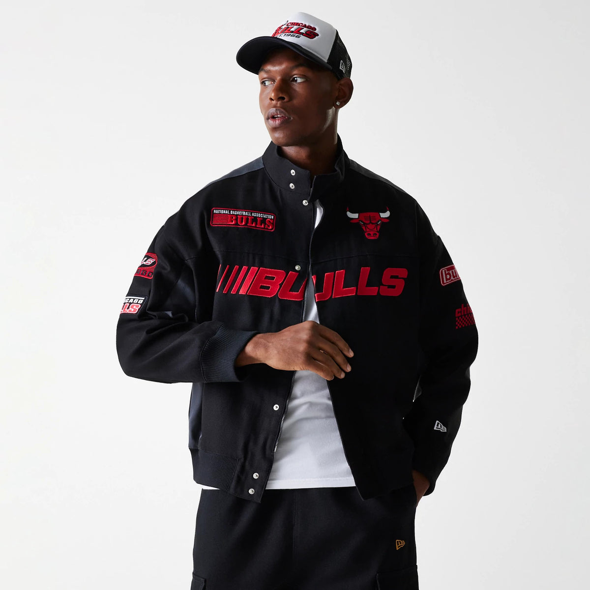 New Era Chicago Bulls NBA Black Motorsports Jacket, on-model view showing a black jacket with red Bulls graphics across the front, a debossed New Era logo on the left cuff, various patches on the sleeves and collar, and a red Bulls logo on the chest.
