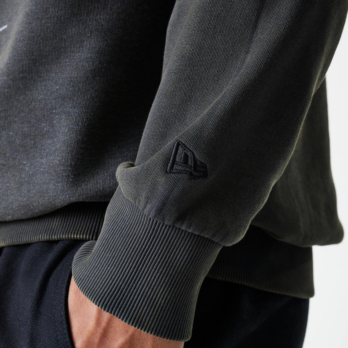 New Era Las Vegas Raiders NFL Washed Super Bowl Grey Oversized Crew Neck Sweater, close-up showing the black New Era flag logo embroidered on the sleeve cuff and the ribbed texture at the wrist.