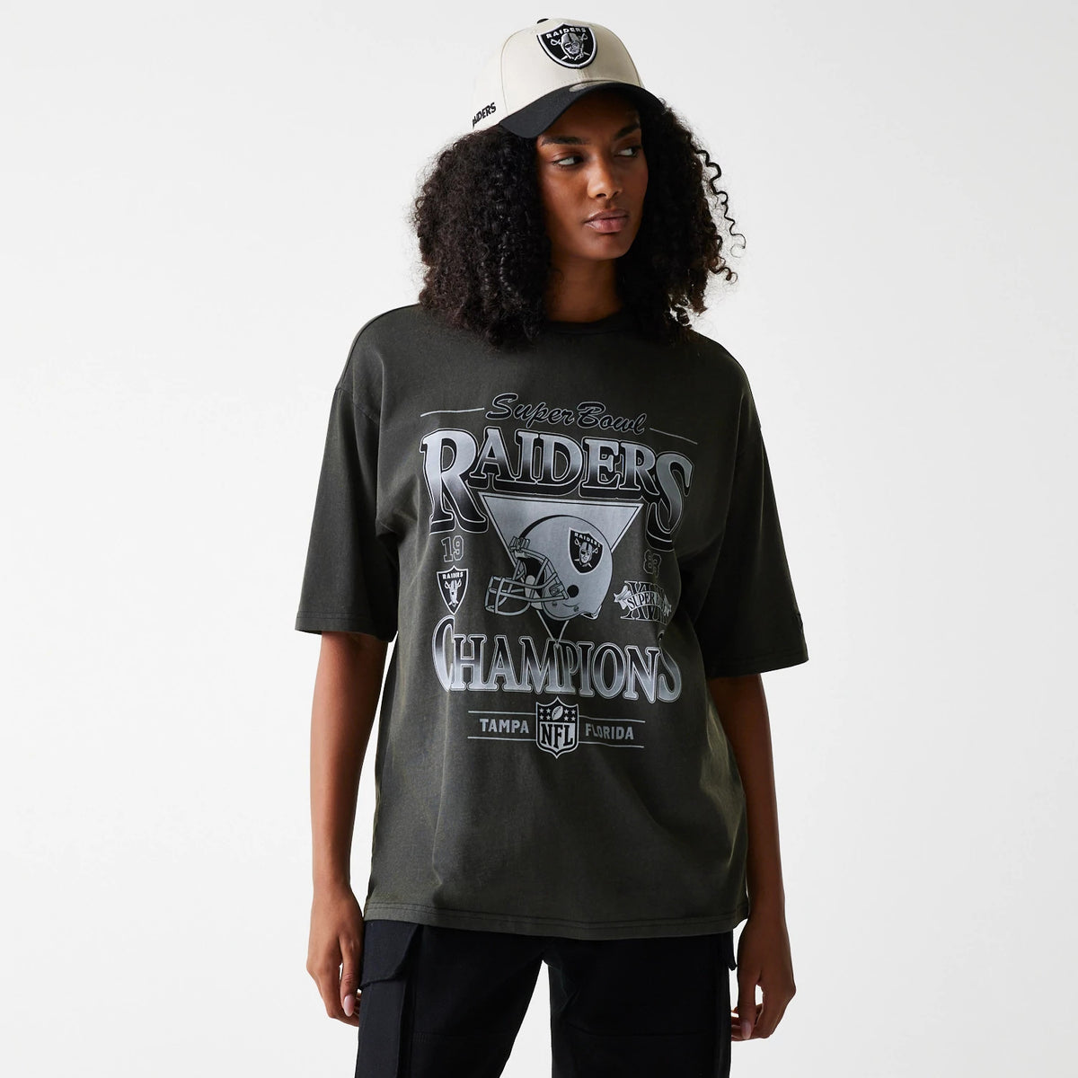New Era Las Vegas Raiders NFL Washed Super Bowl Grey Oversized T-Shirt, on-model view showing a large print of the Raiders logo and Super Bowl Champions text on the front, worn by a person also in a cream cap with a raised Raiders logo.