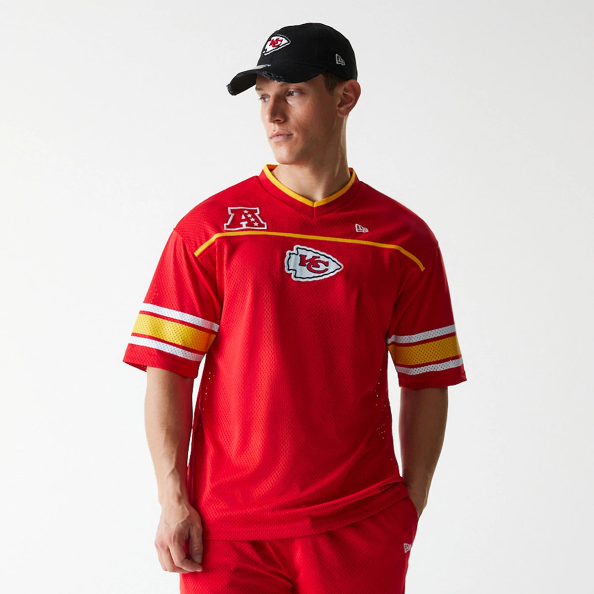 New Era Kansas City Chiefs NFL Mesh Red Jersey, front view on a model wearing a black cap, showcasing the prominent embroidered Chiefs logo on the chest, yellow V-neck detailing, and striped sleeves with AFC patch.