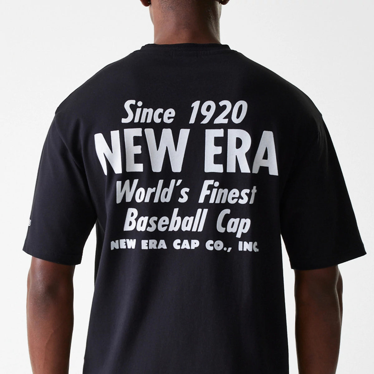 New Era Graphic Black Oversized T-Shirt, rear view showing bold white text across the upper back reading Since 1920 New Era World's Finest Baseball Cap, on a plain black background.