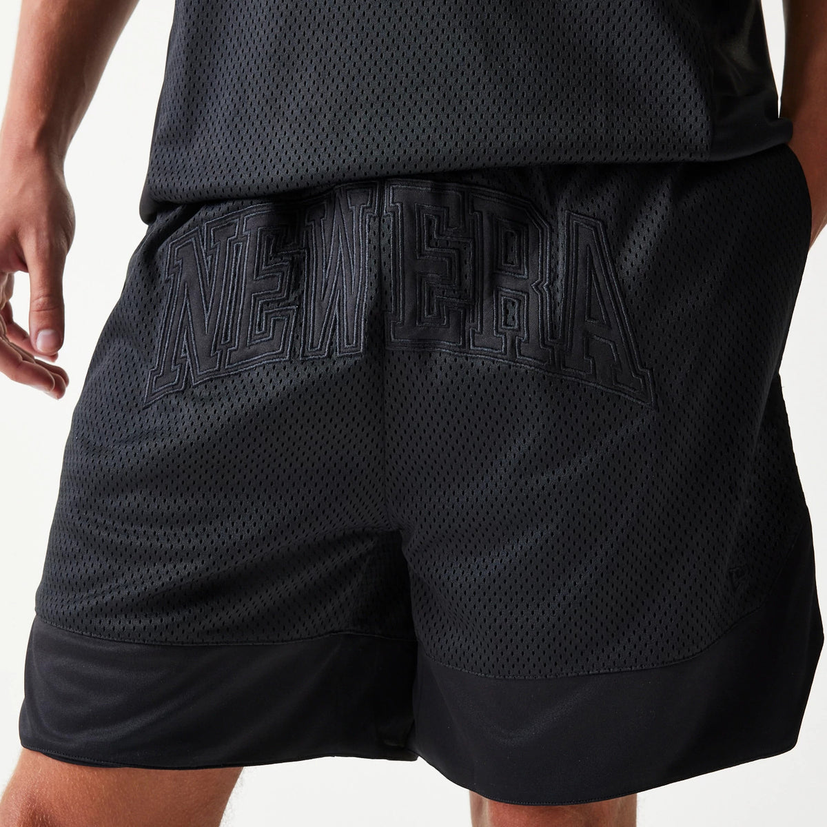 New Era Mesh Black Shorts, rear view showing an embossed New Era logo stretched across the black mesh fabric with a subtle sheen, featuring a wide black band along the hem of each leg.