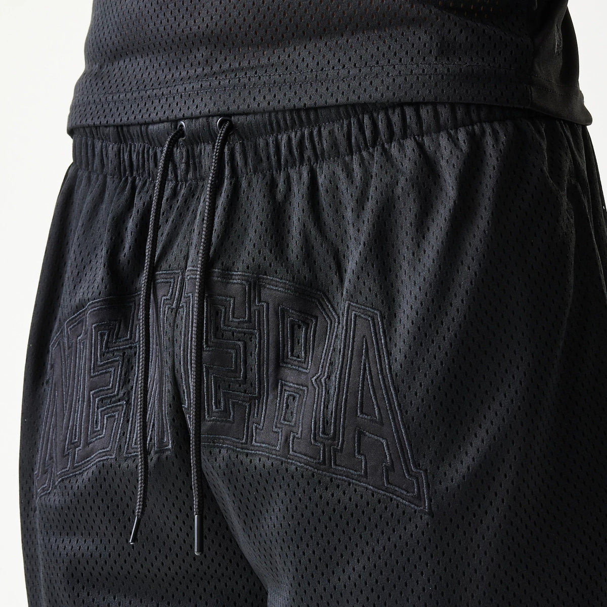 New Era Mesh Black Shorts, side view showing black mesh fabric with an elasticated waistband, drawstrings hanging in front, and a large embossed New Era logo across the back of the shorts.