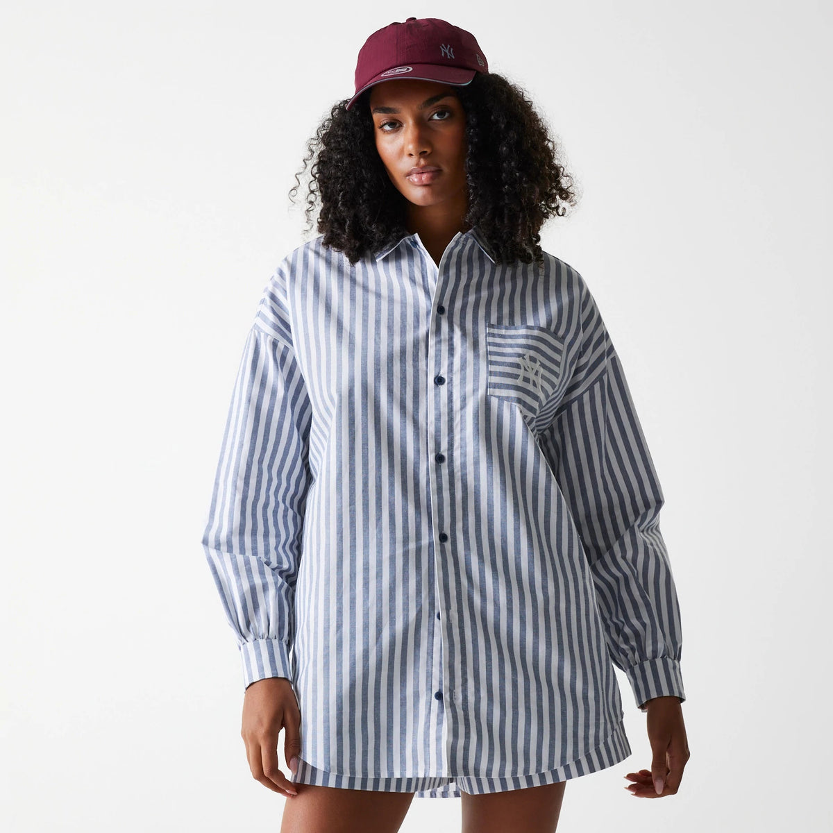 New Era New York Yankees Womens MLB Stripe Dark Blue Long Sleeve Shirt, front view on a model wearing a burgundy cap, featuring vertical blue stripes, a button-down front, and an embroidered Yankees logo on the left chest pocket.