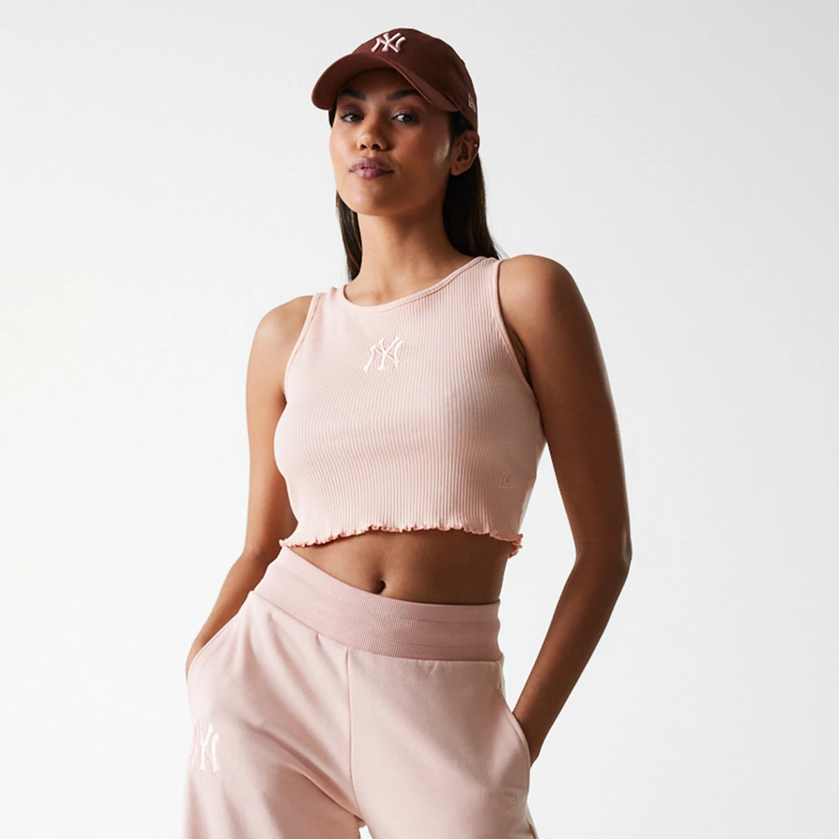 New Era New York Yankees Womens MLB Rib Pastel Pink Rib Tank Top, front view on a model styled with pastel pink joggers, featuring a white embroidered NY logo on the centre chest of the ribbed fabric.