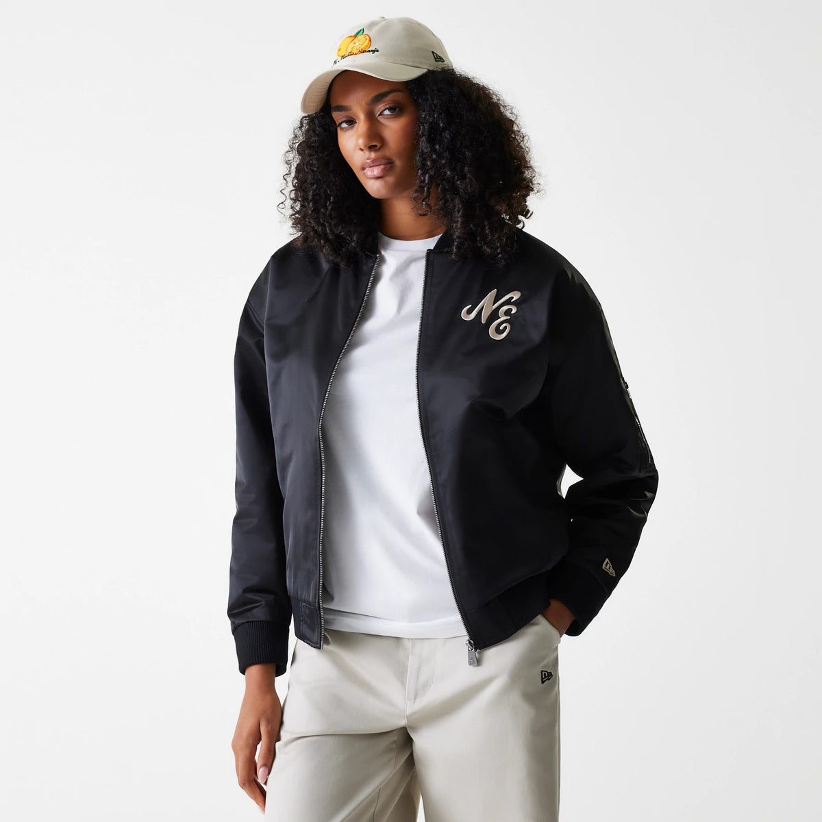 Womens New Era Black Satin Bomber Jacket, on-model view featuring a black satin finish with a raised N logo on the left chest, ribbed cuffs, a front zip closure and a debossed New Era logo on the left sleeve.