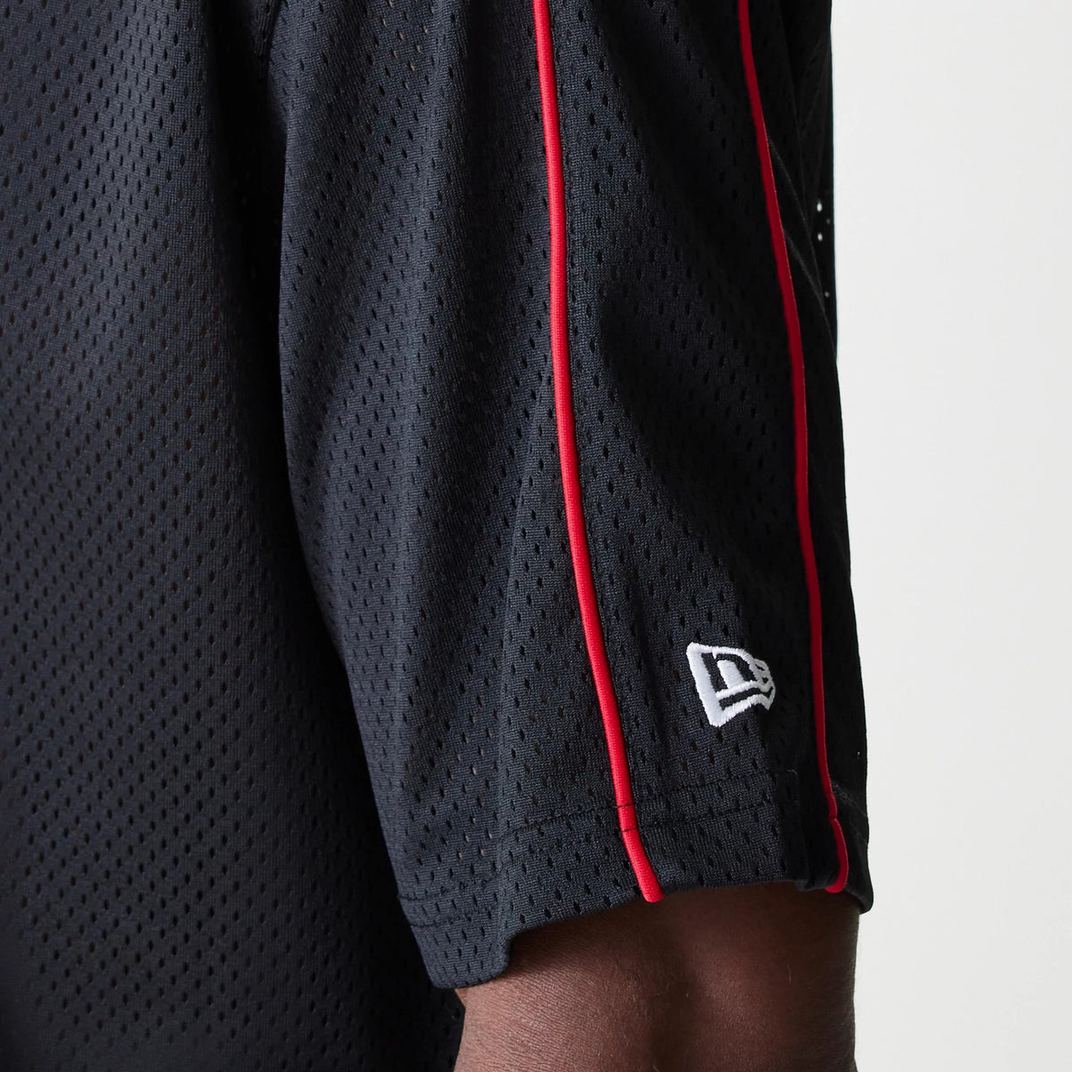 New Era Chicago Bulls NBA Piping Black Oversized Mesh T-Shirt, side view showing the black mesh fabric with distinctive red piping along the sleeve, featuring a raised New Era logo embroidered in white near the hem.