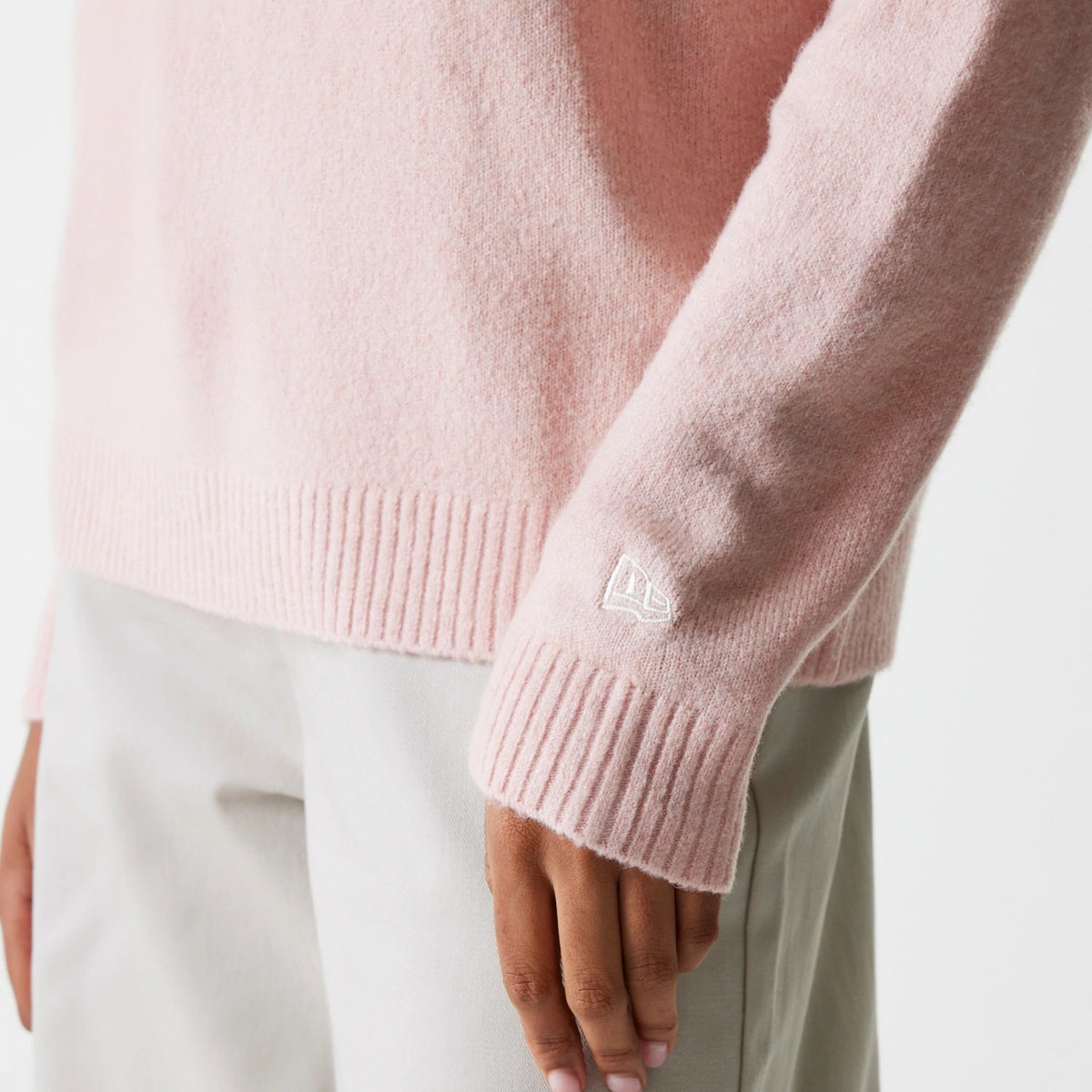 New Era New York Yankees Womens MLB Knit Pastel Pink Crew Neck Sweater, close-up of the lower sleeve and hem showing the New Era flag logo embroidered in white on the ribbed cuff, worn with light grey trousers.