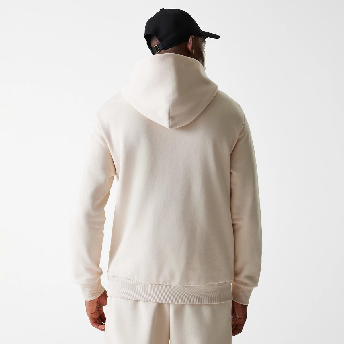 New Era Tech Light Beige Oversized Pullover Hoodie, rear view showing the hood resting on the back shoulders and straight hemline, with long sleeves extending down the arms against the light beige fabric.