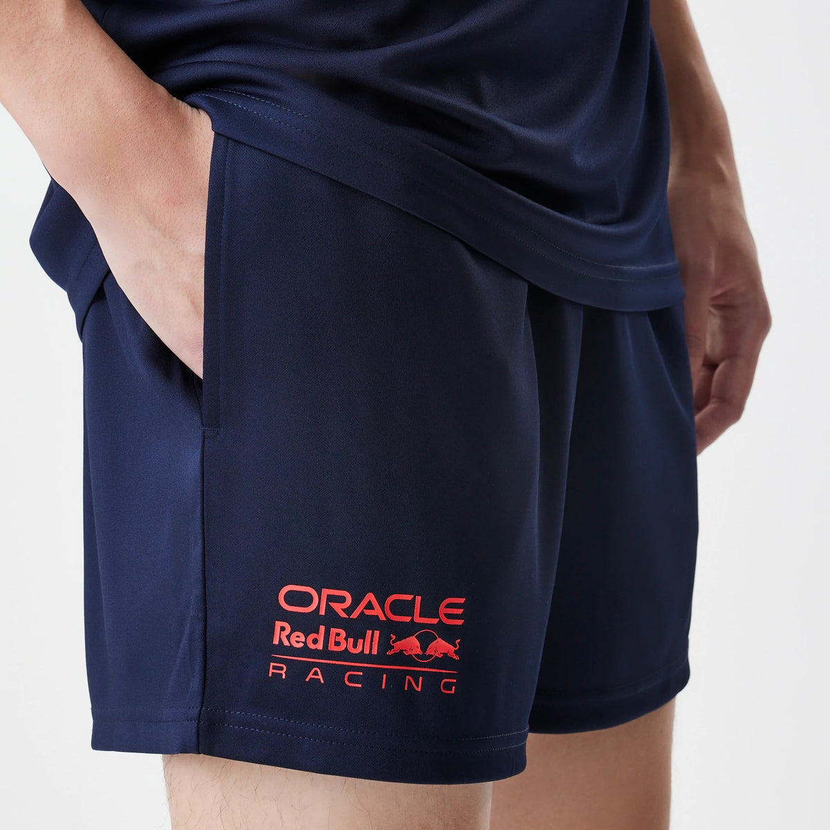 New Era Red Bull Racing Graphic Dark Blue Football Shorts, front view on-model showing the red embroidered Oracle Red Bull Racing logo near the hem on the left leg, alongside the dark blue fabric and relaxed fit.