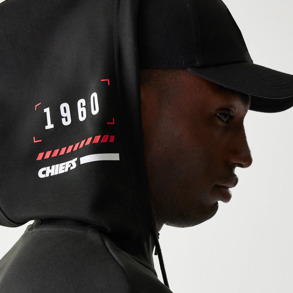 New Era Kansas City Chiefs NFL 3RD Down Black Pullover Hoodie, side view showing a black hood with printed '1960' in white and red graphics along with 'CHIEFS' text, displayed on-model with a matching black cap.