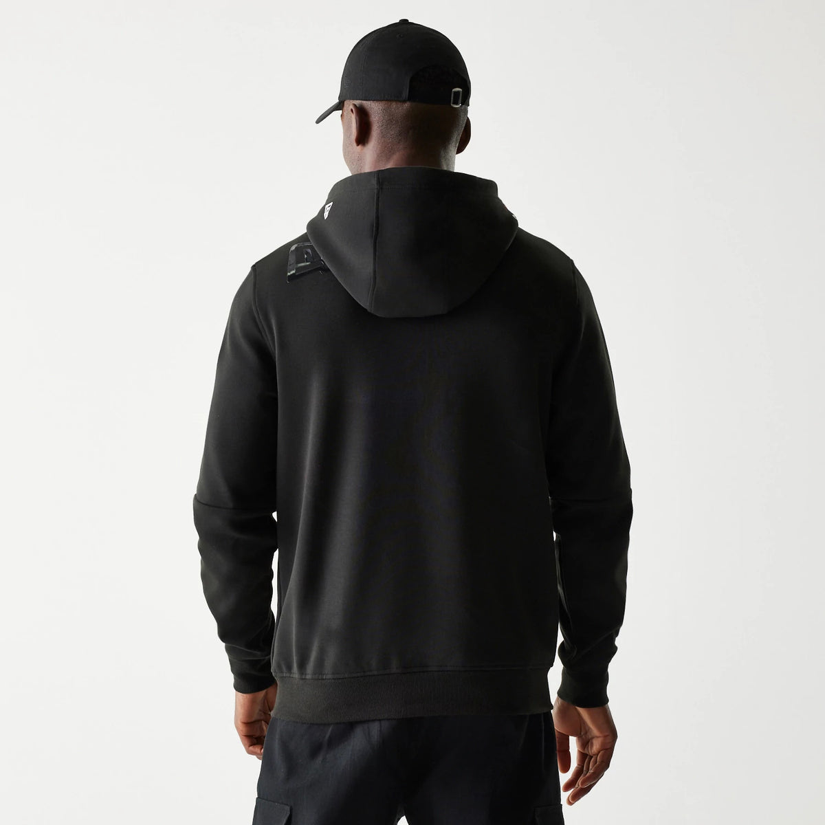 New Era Kansas City Chiefs NFL 3RD Down Black Pullover Hoodie, back view on a model with a matching cap, showing the plain black design with a small embroidered New Era logo on the hood near the left shoulder.