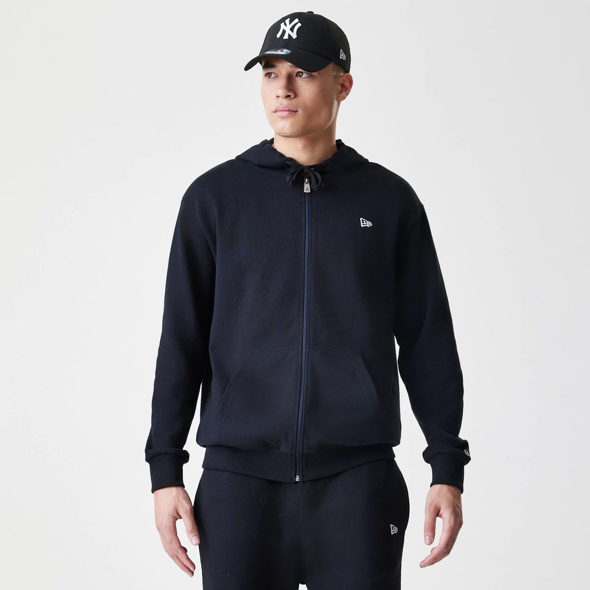 The Male model is wearing New Era Premium Essential Black Oversized Full Zip Hoodie 1