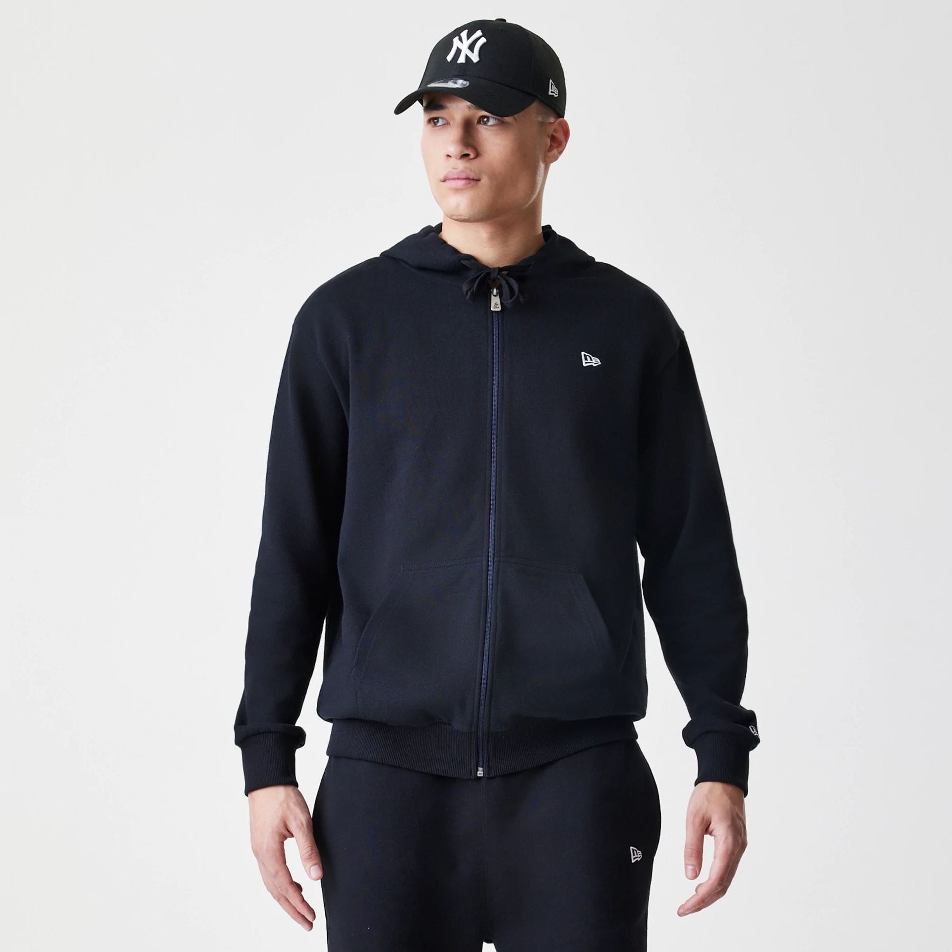 The Male model is wearing New Era Premium Essential Black Oversized Full Zip Hoodie 1