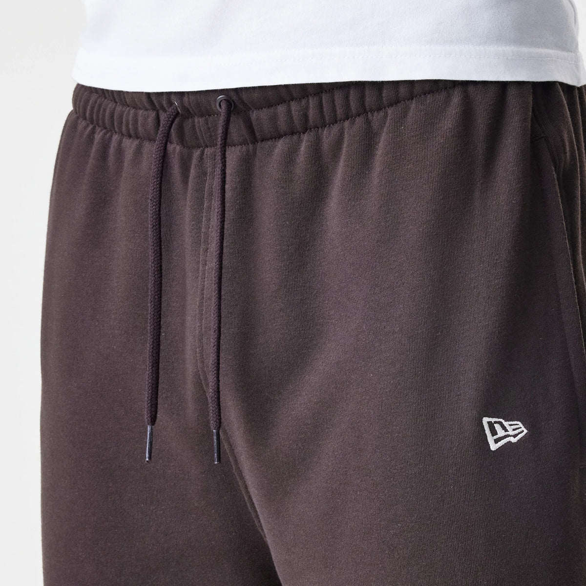 New Era New York Yankees MLB Midi League Essential Dark Brown Joggers, close-up view showing the elasticated waistband with drawstring, and the white embroidered New Era flag logo on the left thigh.