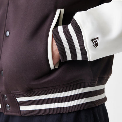New Era New York Yankees MLB Dark Brown Varsity Jacket, close-up showing the side view of a brown body with white sleeves, a striped ribbed cuff and waistband, and an embroidered logo near the wrist.