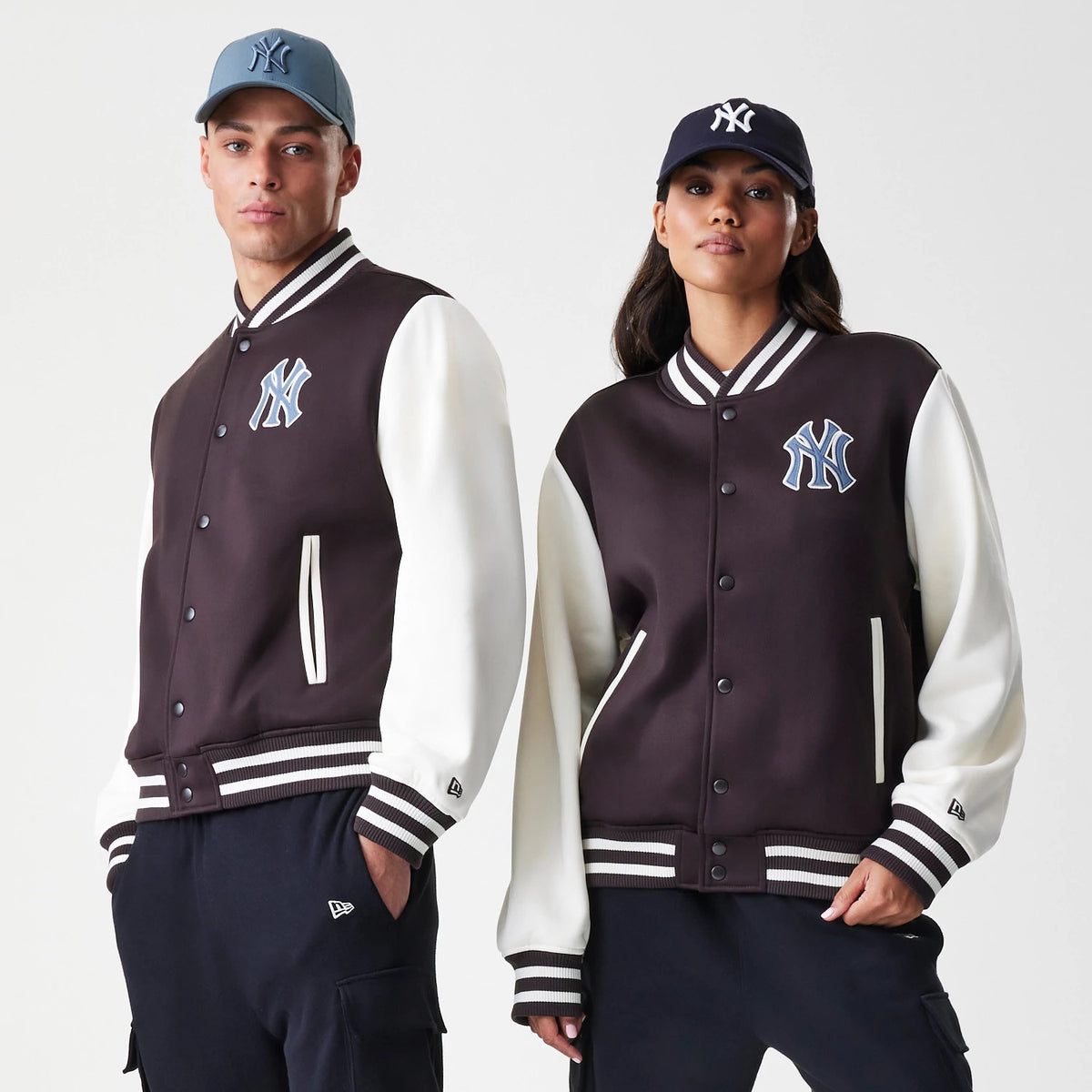 New Era New York Yankees MLB Dark Brown Varsity Jacket, front on-model view showing the dark brown body with white sleeves, an embroidered Yankees logo on the chest, and striped ribbed cuffs, hem and collar, styled with matching caps.