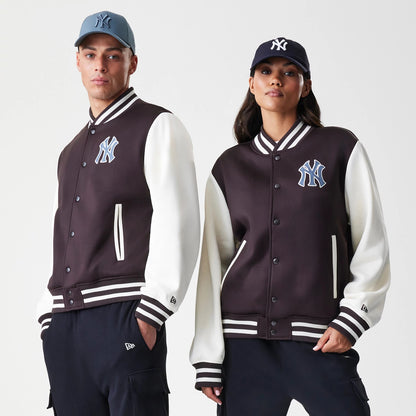 New Era New York Yankees MLB Dark Brown Varsity Jacket, front on-model view showing the dark brown body with white sleeves, an embroidered Yankees logo on the chest, and striped ribbed cuffs, hem and collar, styled with matching caps.