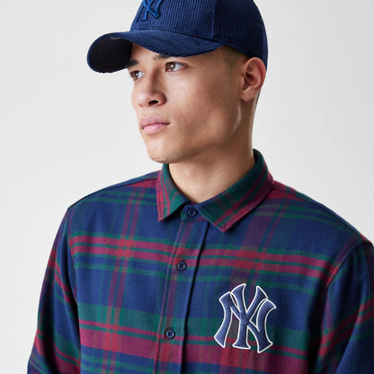 New Era New York Yankees MLB Check Navy Long Sleeve Shirt, front view on a model wearing a matching navy corduroy cap, featuring a large white embroidered Yankees logo on the left chest and a button-up plaid design in navy, red, and green.