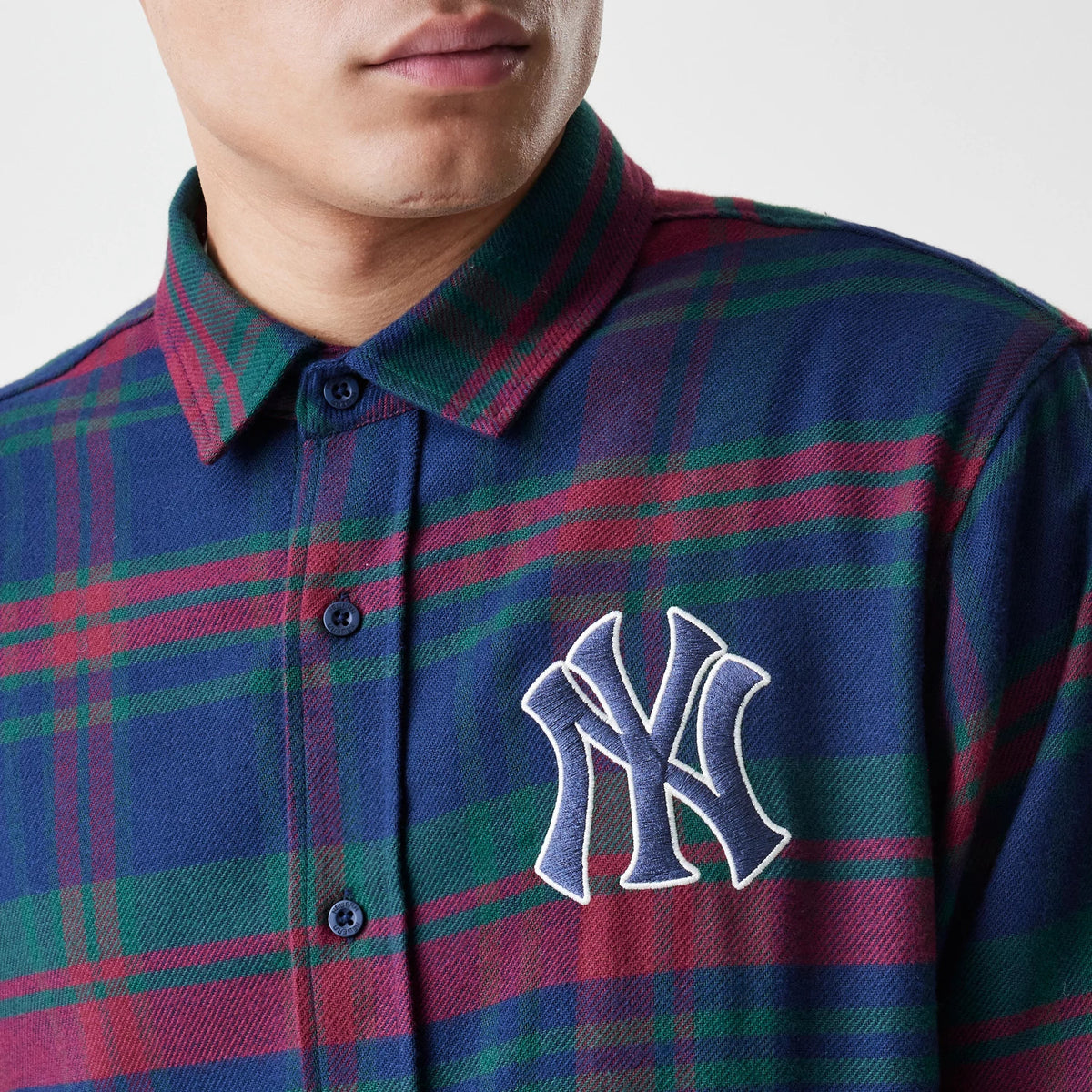 New Era New York Yankees MLB Check Navy Long Sleeve Shirt, front view on a model showcasing a blue and red check pattern with a prominent white-outlined NY logo embroidered on the left chest.