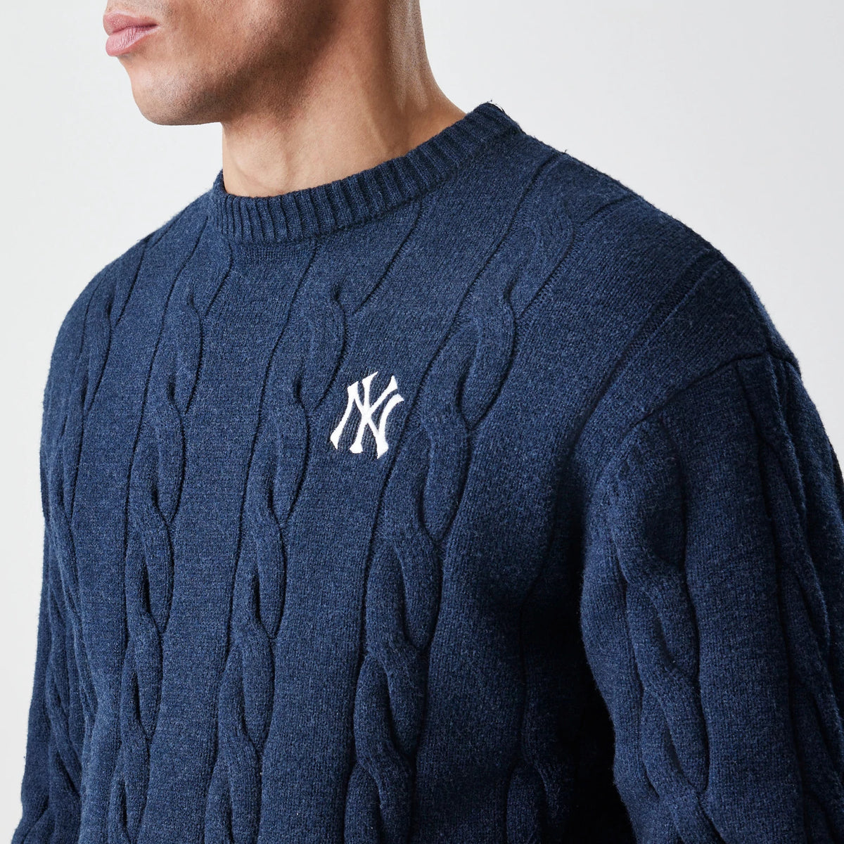 New Era New York Yankees MLB Cable Knit Navy Knitted Sweater, side view on a model showing the textured cable knit pattern with an embroidered white NY logo on the chest and a ribbed crew neck.