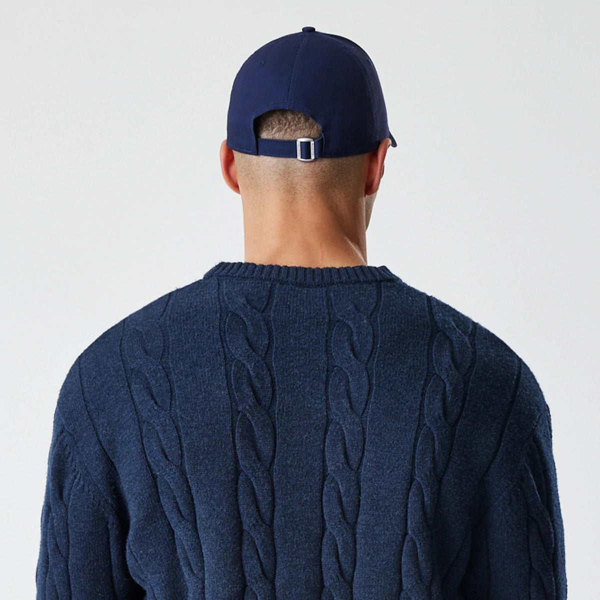 New Era New York Yankees MLB Cable Knit Navy Knitted Sweater, rear view on a model with a plain navy cap, showcasing the intricate cable knit pattern on the back and ribbed neckline of the sweater.