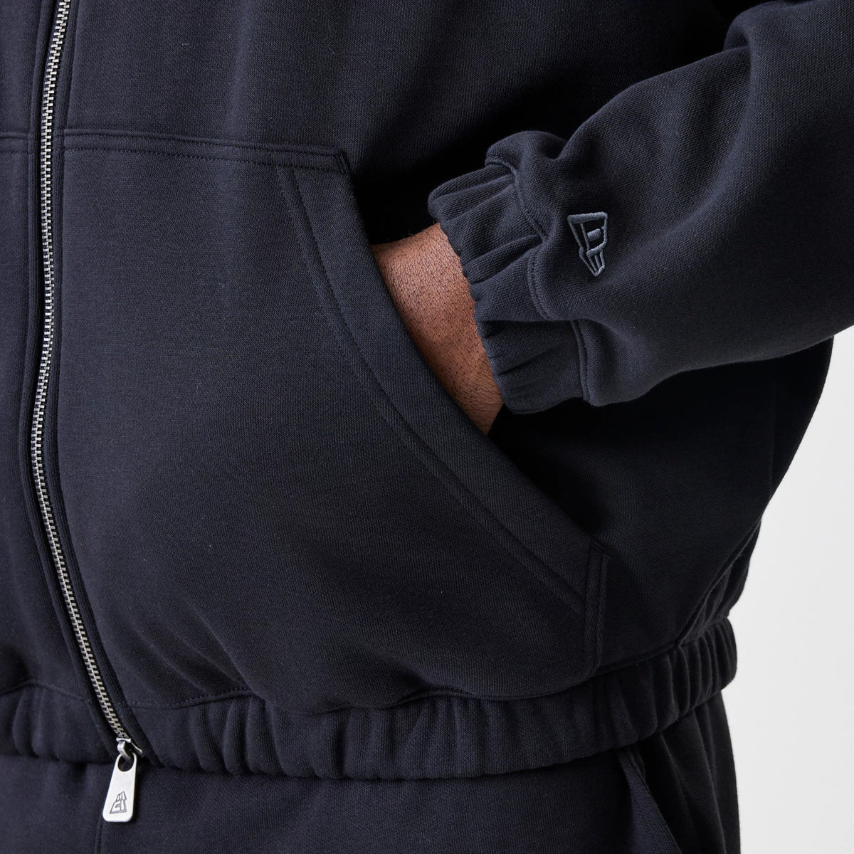 New Era Chicago Bulls NBA Linear Black Oversized Full Zip Hoodie, side view showing the silver zip detail, a hand in the front pocket and a small embroidered New Era logo on the sleeve near the wrist.