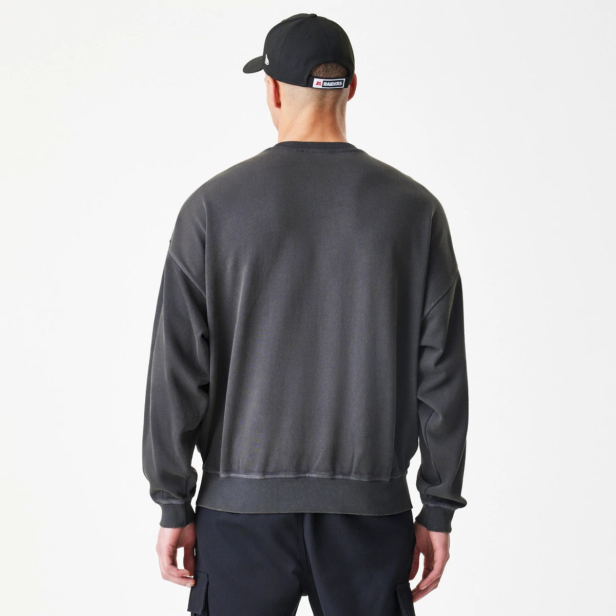 New Era Las Vegas Raiders NFL Washed Boxy Dark Grey Oversized Crew Neck Sweater, back view on a model wearing a black cap, showing the relaxed fit with long sleeves and ribbing at the cuffs and hem in dark grey.