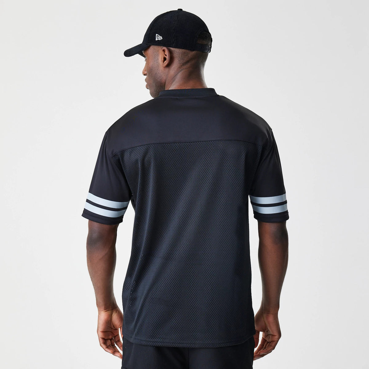 New Era Las Vegas Raiders NFL Script Mesh Black Jersey, back view on a model wearing a black cap, showing a mesh lower panel, solid shoulder yoke, and two white horizontal stripes on each sleeve.