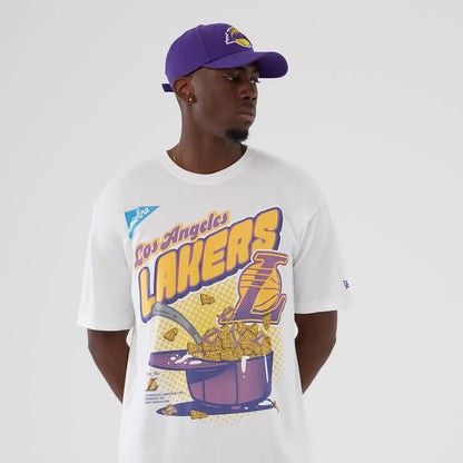 New Era LA Lakers NBA Lifestyle Graphic White T-Shirt, front view on a model with a purple cap showing a graphic of the Lakers' logo, a basketball theme in purple and yellow with Los Angeles Lakers text, and a New Era logo label on the sleeve.