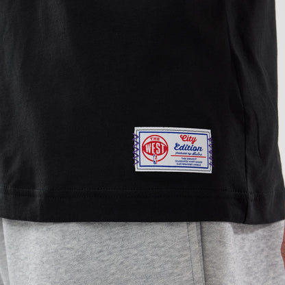 New Era LA Lakers NBA City Edition Black T-Shirt, side view showing a label near the hem with The West and City Edition in red and blue on white, contrasting against the solid black fabric of the T-shirt.