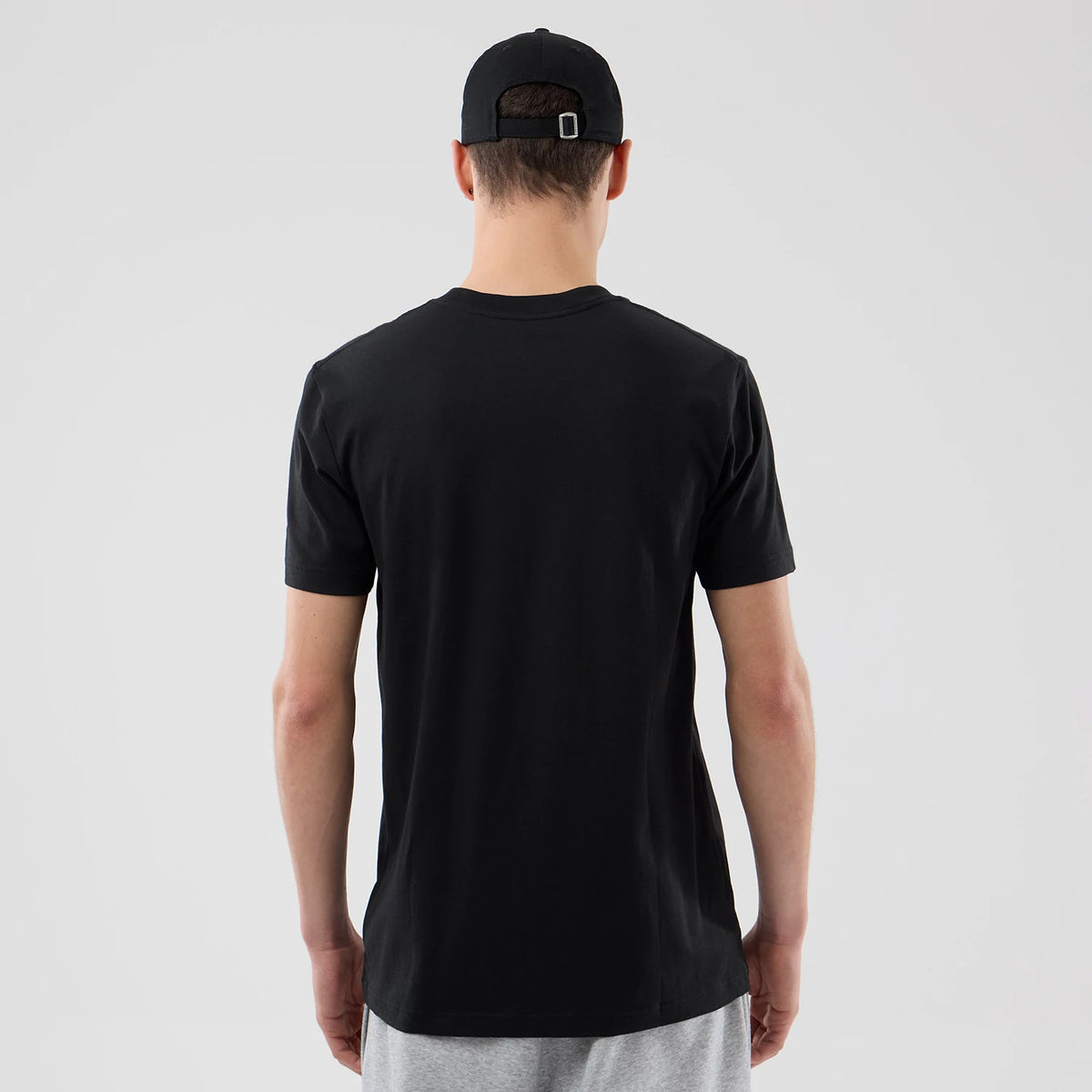 New Era LA Lakers NBA City Edition Black T-Shirt, back view on-model showing a plain black design with short sleeves, paired with light grey shorts and a black cap featuring an adjustable strap at the back.