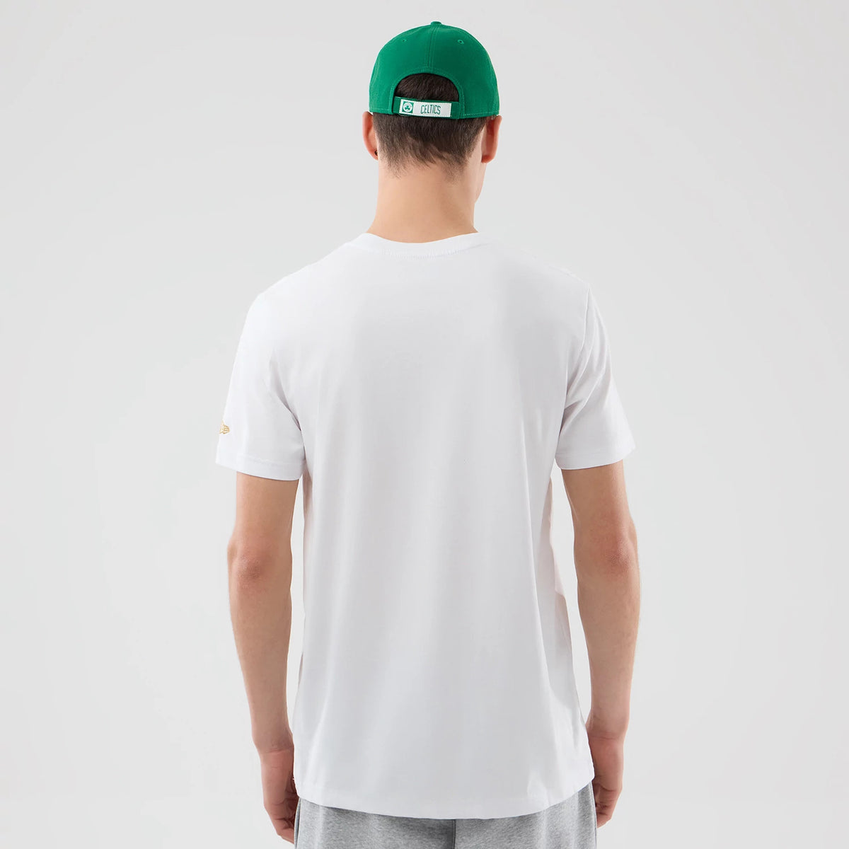 New Era Boston Celtics NBA City Edition White T-Shirt, back view on a model with a green cap, showing the plain white back and short sleeves with a small embroidered NBA logo on the right sleeve near the shoulder.