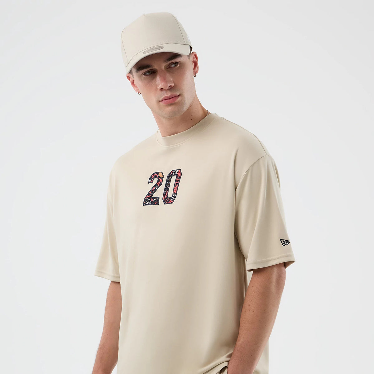 New Era Mesh Infill Light Beige Oversized T-Shirt, front view on a model wearing a matching cap, showcasing a floral-patterned number 20 on the chest and a small embroidered New Era logo on the left sleeve.