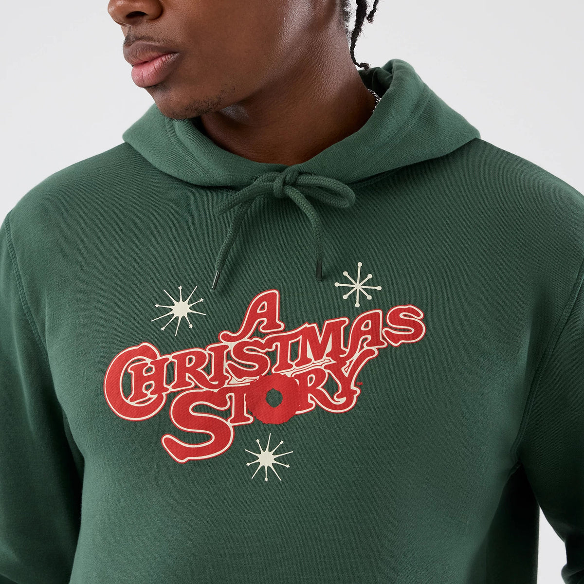 New Era A Christmas Story Major Award Dark Green Pullover Hoodie, front view showing red printed A Christmas Story lettering with cream star details across the chest, worn by a model who is styled casually.