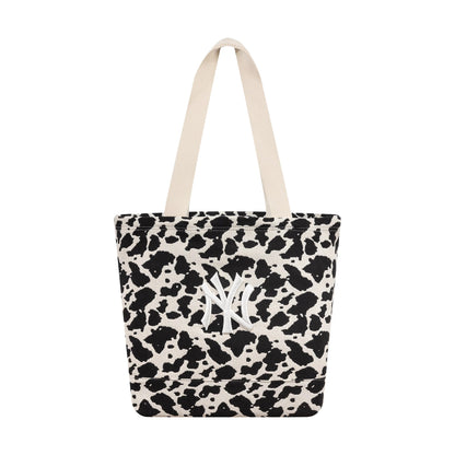 New Era New York Yankees MLB Cow Jacquard Cream Tote Bag, front view showing a cow print design with black and cream spots, dual cream handles at the top, and an embroidered white New York Yankees logo on the side of the tote.