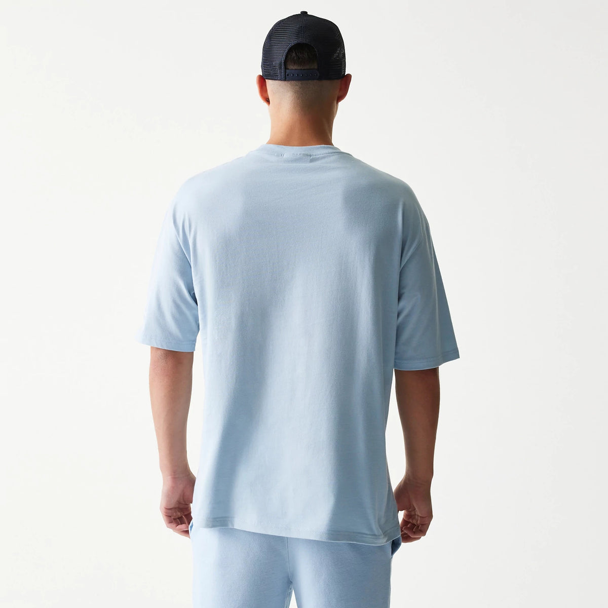 New Era New York Yankees MLB Midi Pastel Blue Oversized T-Shirt, back view on a model wearing a coordinating cap, showing the plain light blue fabric with extended sleeves and a relaxed fit of the oversized design.