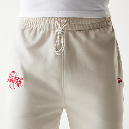 New Era LA Lakers NBA League Essential Cream Joggers, front view showing the red Lakers logo embroidery on the left leg, elasticated waistband with drawstring, and New Era flag logo on the right side.