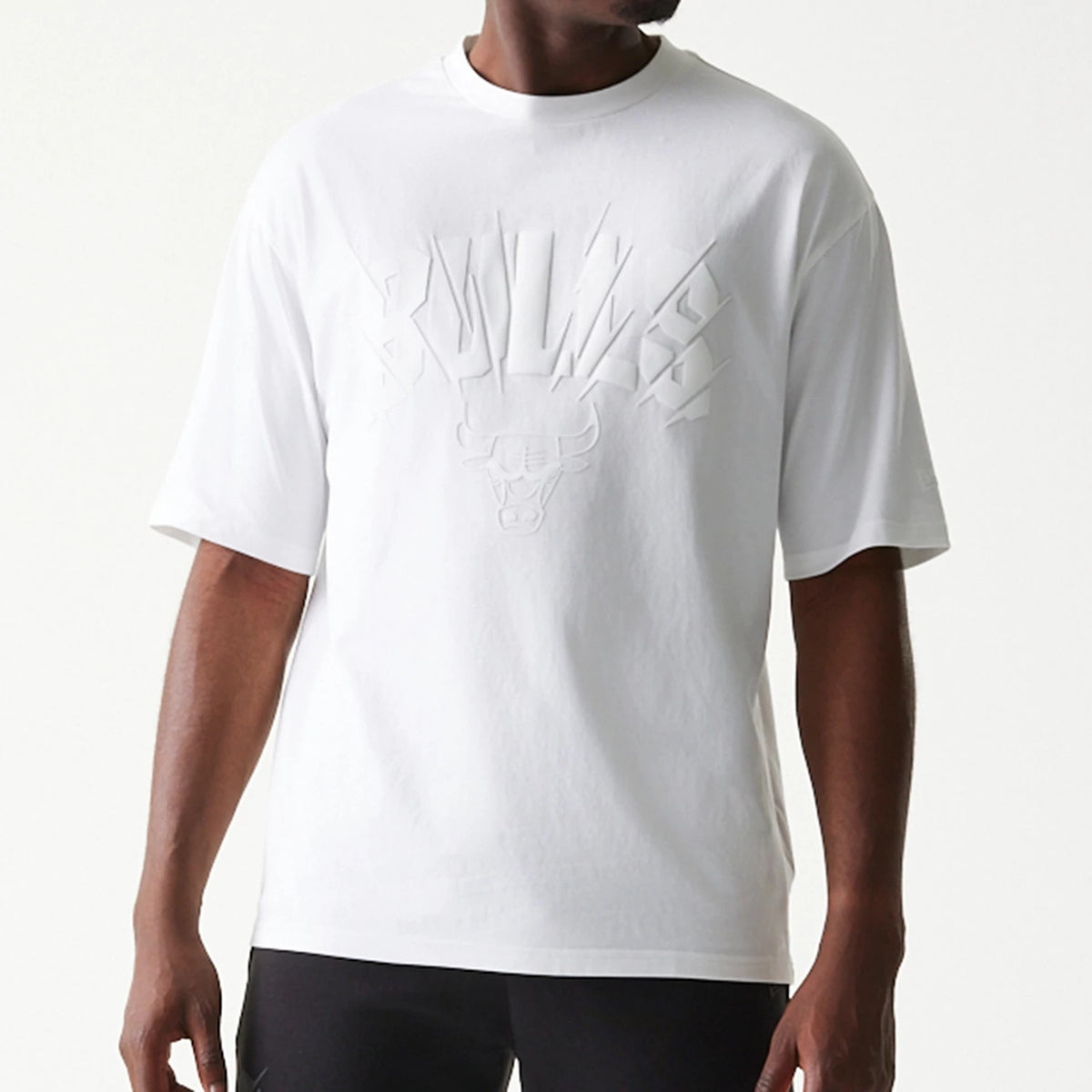 New Era Chicago Bulls NBA White Oversized T-Shirt, front view on a model showing a embossed Bulls logo and lettering across the chest, short sleeves, and a relaxed fit design in plain white.