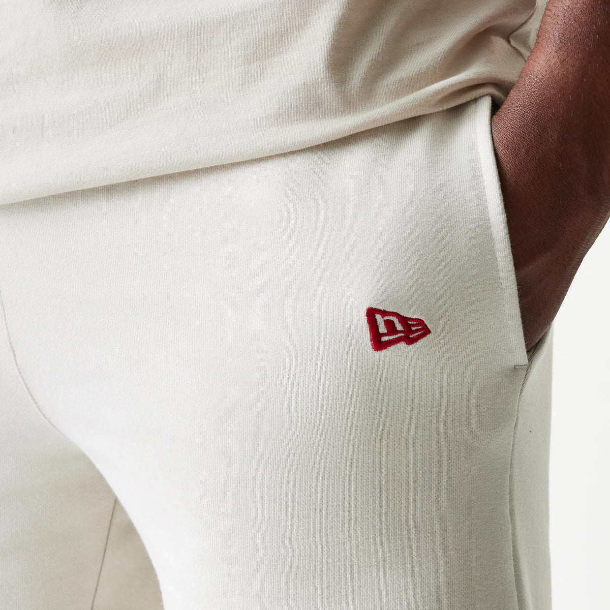 New Era LA Lakers NBA League Essential Cream Shorts, three-quarter view showing an embroidered red New Era logo near the pocket on a cream fabric, worn on a model with a matching top for a coordinated look.